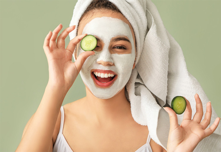 Woman holding a cucumber slice to her eye.