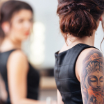 Woman with arm tattoos looking in a mirror.