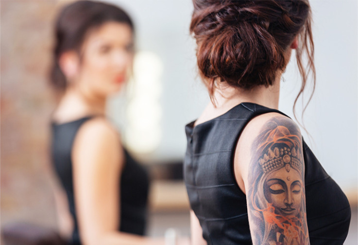 Woman with arm tattoos looking in a mirror.