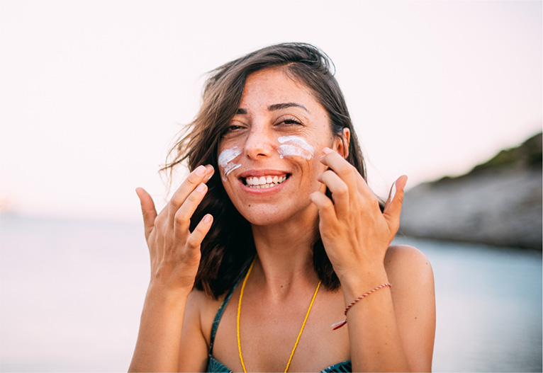 Smiling woman applying sunscreen to her cheeks.