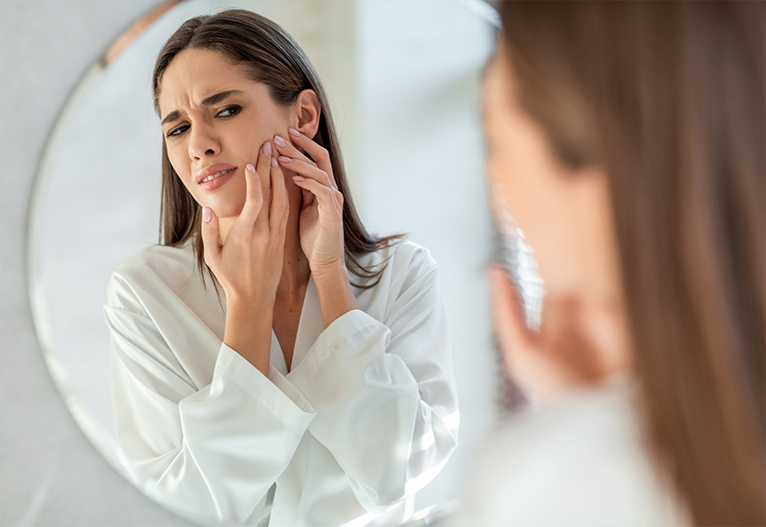 Woman with problem skin looking in the mirror.