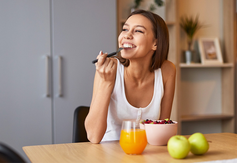 A smiling woman eating healthy food at a table.