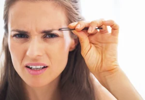 Woman plucking eyebrows while grimmacing.