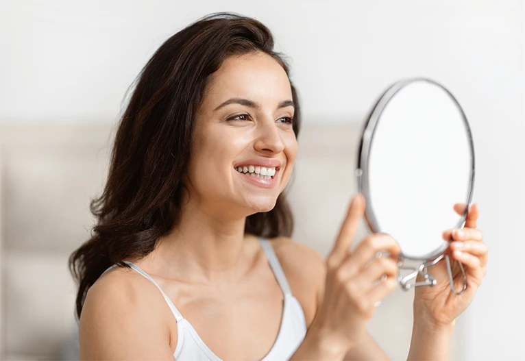 Woman smiling as she looks in a makeup mirror.