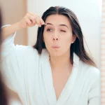 Woman plucking her eyebrows in the mirror.