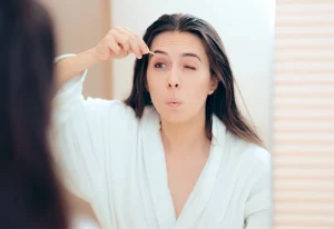 Woman plucking her eyebrows in the mirror.